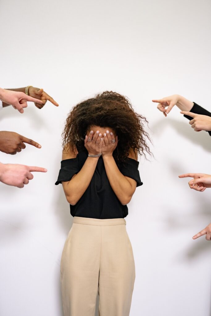 Bullied woman covers face A bullied woman covers her face as multiple hands point accusatorily in a studio setting.