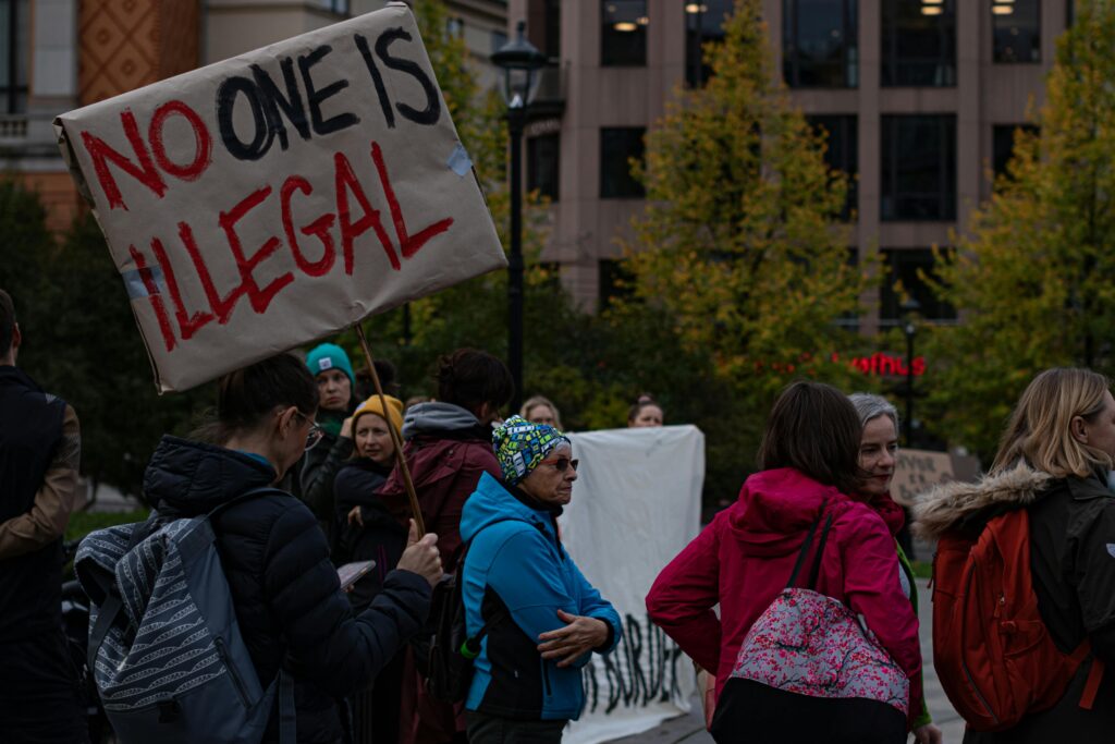 being an immigrant means being a scapegoat A group of diverse adults protesting immigration policies with signs outdoors.